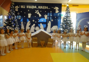Dziewczynki przebrane za aniołki stoją wokół szopki ze złożonymi rączkami